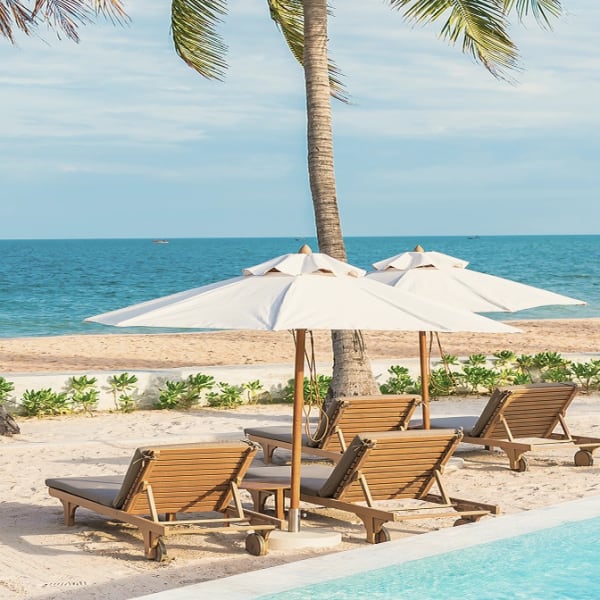 Sun loungers and parasols on the sand beside the pool at the beach club
